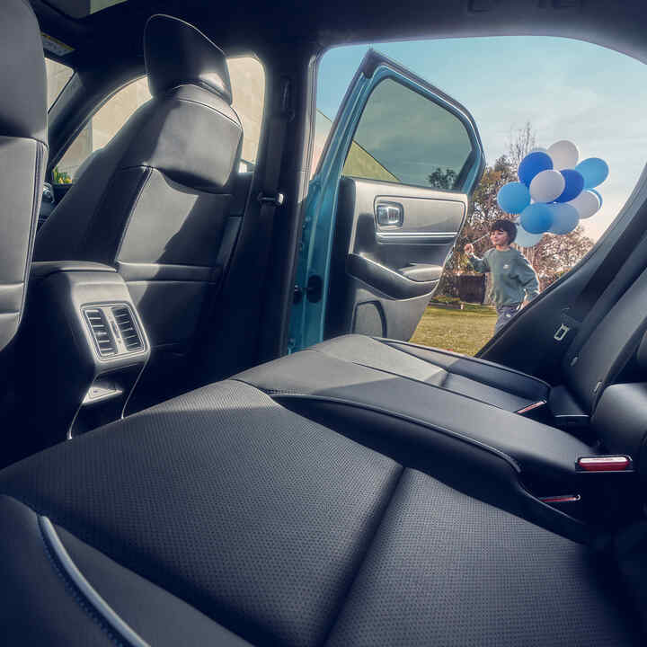 Close up of the rear seat in the Honda e:Ny1 with child walking past open door carrying balloons.