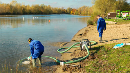 High flow rate/trash being used by workers in blue overalls in a lake location.