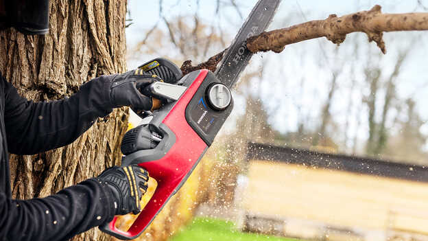 Close up of model cutting a tree branch with a Cordless Chainsaw.