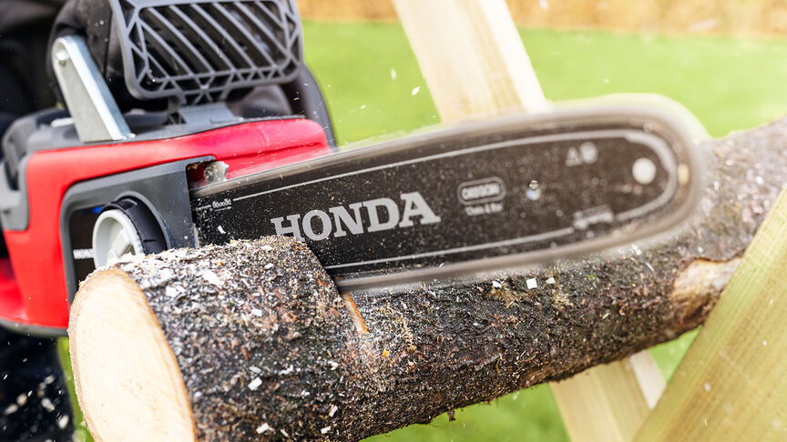 Close up of a model cutting wood with a Honda cordless chainsaw.