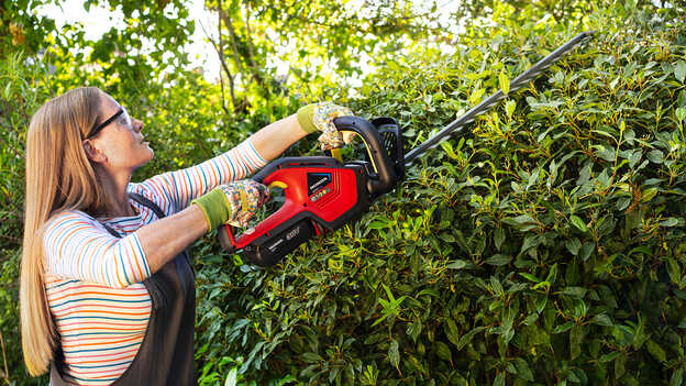 Woman trimming bushes with Honda Cordless Hedgetrimmer in a garden location.