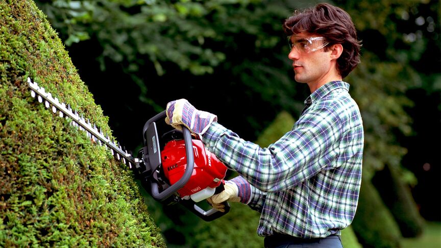 Man using hedgetrimmer with noise cancellation headphones