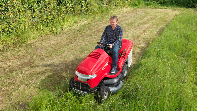 Premium lawn tractor, front three-quarter, left facing, being used by model, garden location.