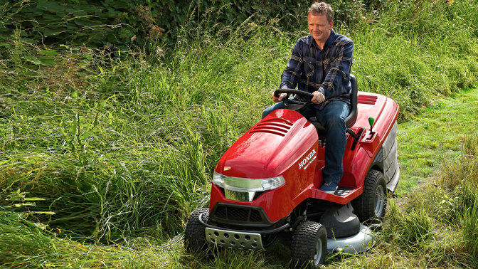 Front three-quarter, left facing premium lawn tractor, being used by model, garden location.