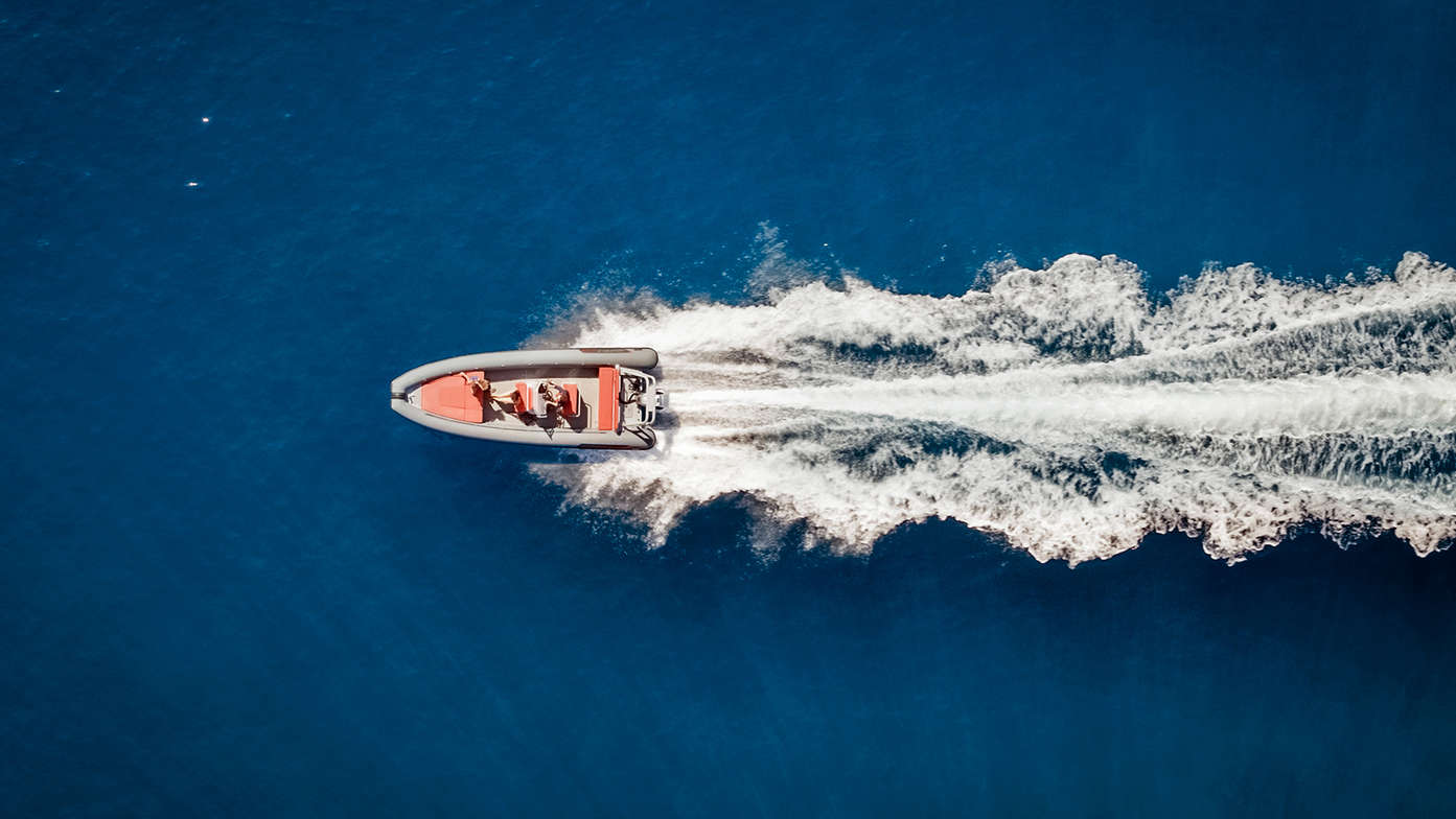 distant aerial view of a people steering a boat with the wake of the boat behind them