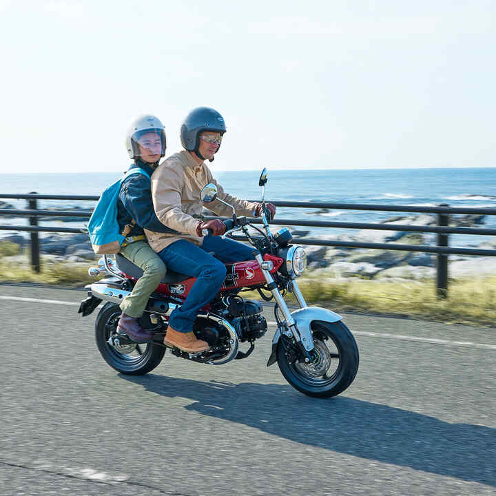 Honda Dax 125 on coastal road with rider and pillion