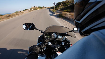 Over the rider's shoulder view of motorcycle instruments, handlebars and the road ahead (Location).