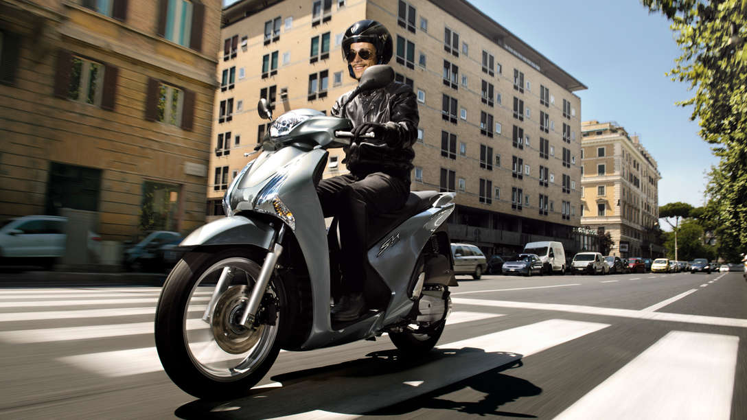 Honda SH125i motorbike front-threequarter view with rider. Left-facing (Road location).