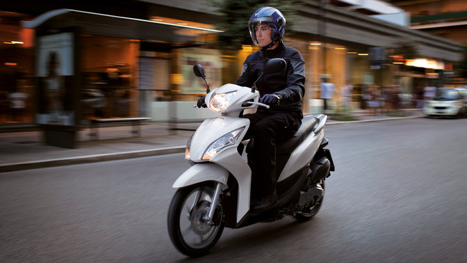 White Honda Vision scooter front-threequarter view with rider. Left-facing (Road location).