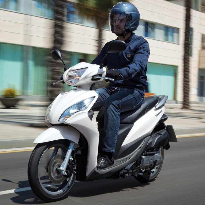 White Honda Vision scooter front-threequarter view with rider. Left-facing (Road location).