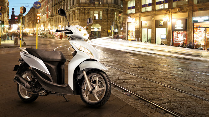 Front, 3-quarter view of Vision scooter, red, on stand in evening urban location.