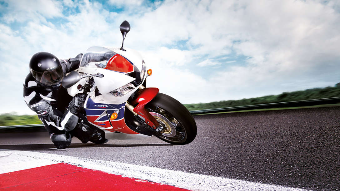 Honda CBR600RR motorbike front-threequarter view with rider, leaning into bend. Right-facing (Race track location).