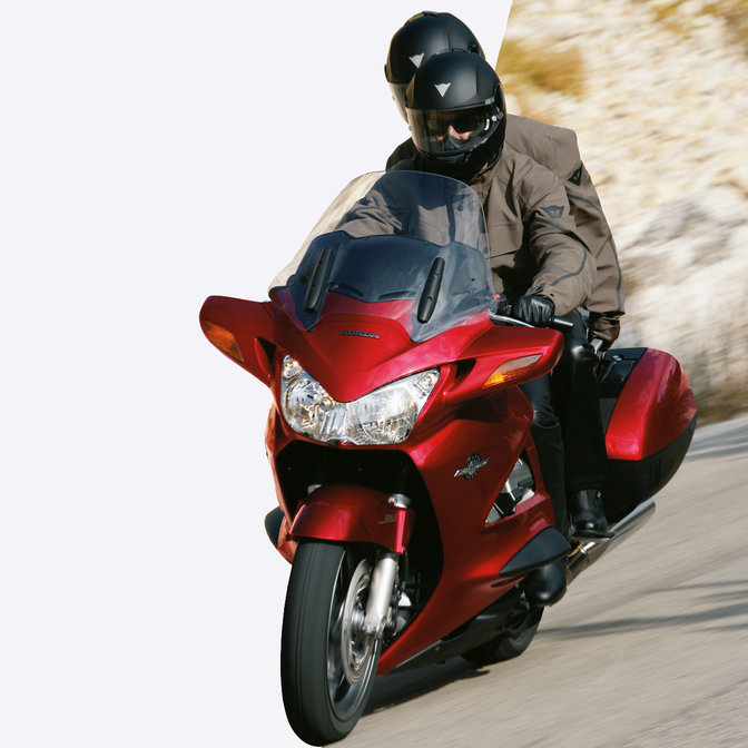 Front, 3 quarter facing red Pan-European with rider and pillion, road location, left facing.