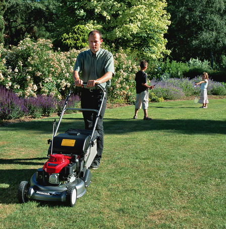 Front three-quarter lawnmower, being used by model, garden location.