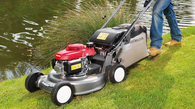 Honda HRD lawnmower with large fuel tank mowing grass in garden location.