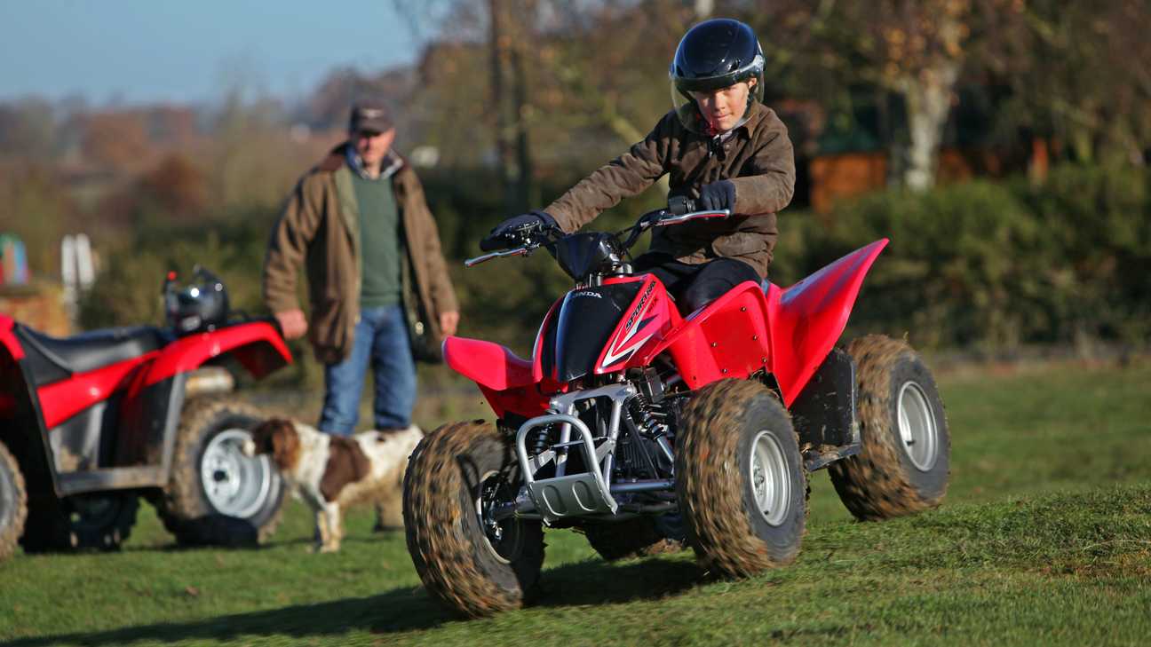 Honda trx90x sportrax being ridden by child in a field.