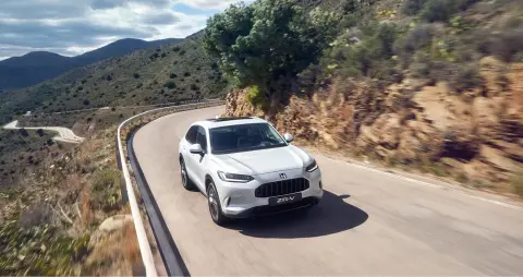A white 27YM ZR-V driving around a mountain, on a mountain road, front facing. 