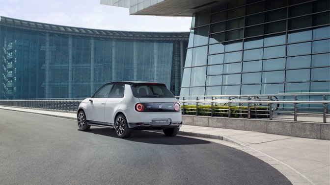 Rear three-quarter view honda e with glass buildings in the background