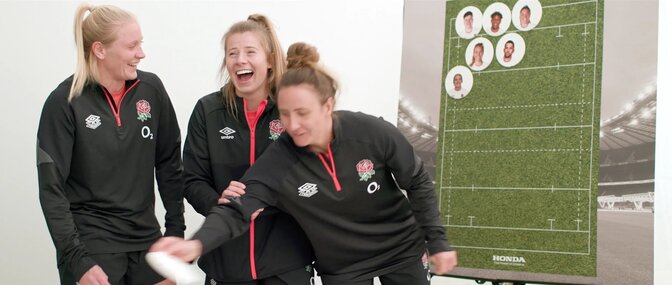 Three members of Red Roses team next to rugby pitch mock up.