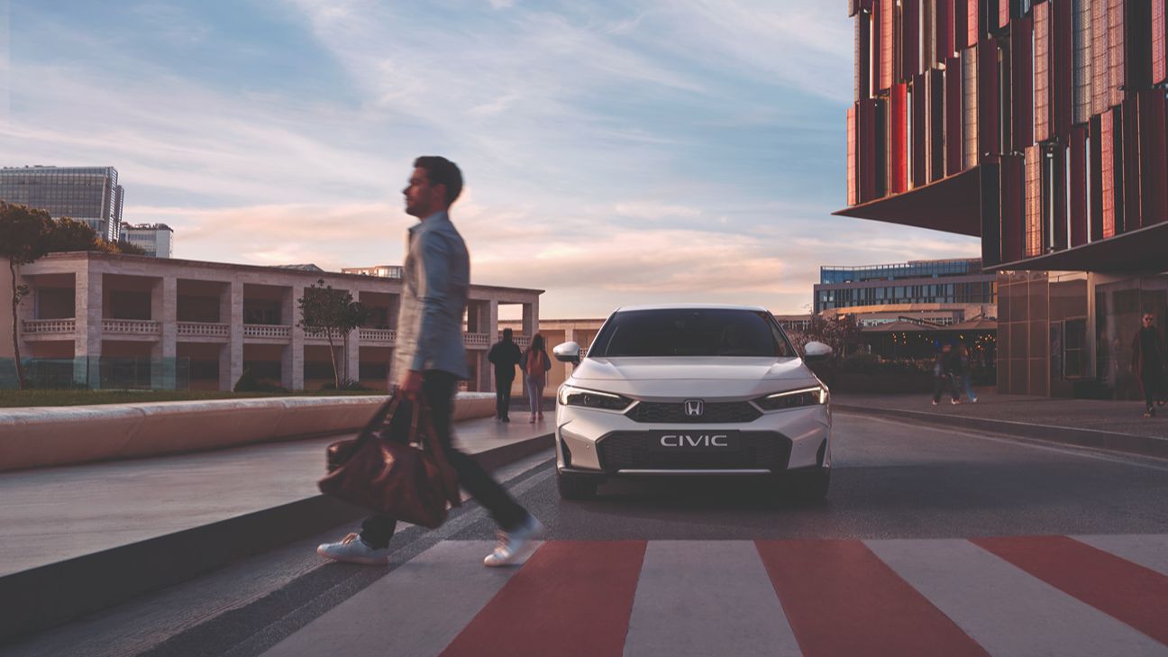 a man crossing the street with a white Honda Civic in the back