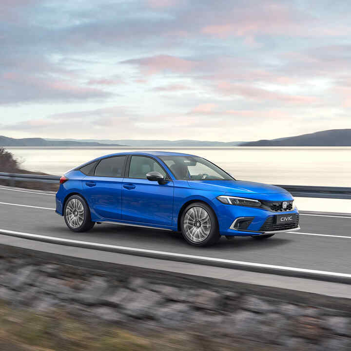 Front three quarter Honda Civic e:HEV driving down a coastal road.