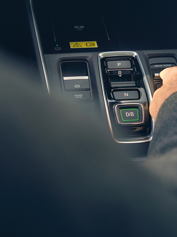 A person's hand reaching to adjust a toggle switch on a modern car's center console next to the gear selector buttons.