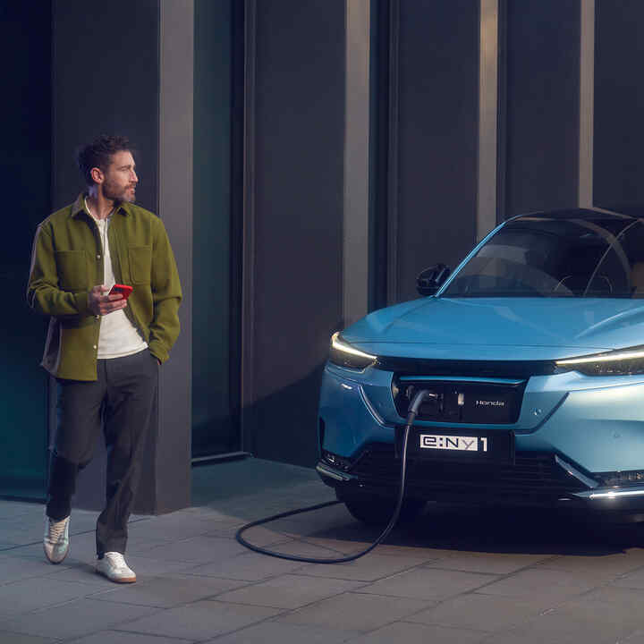 Man walking next to front facing Honda e:Ny1 plugged in and charging.