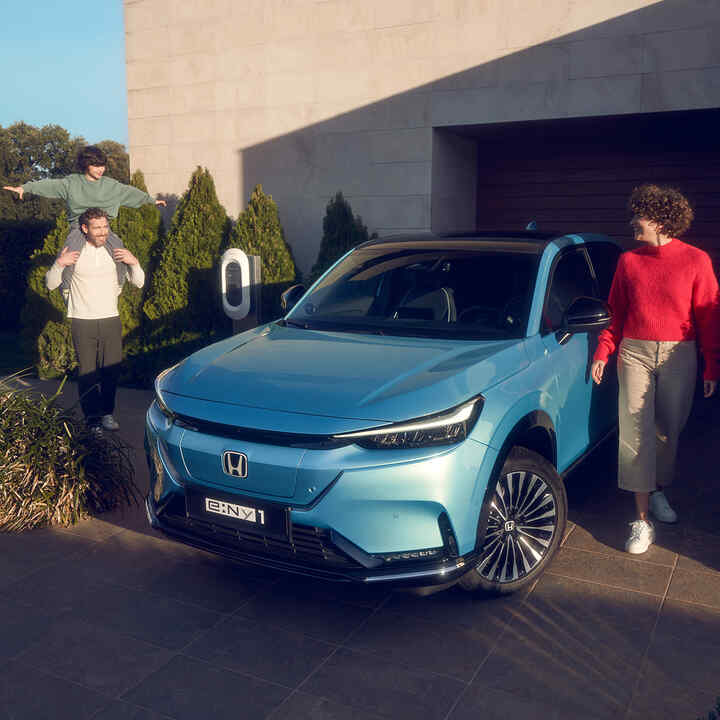 Family standing next to Front facing Honda e:Ny1 parked outside house.