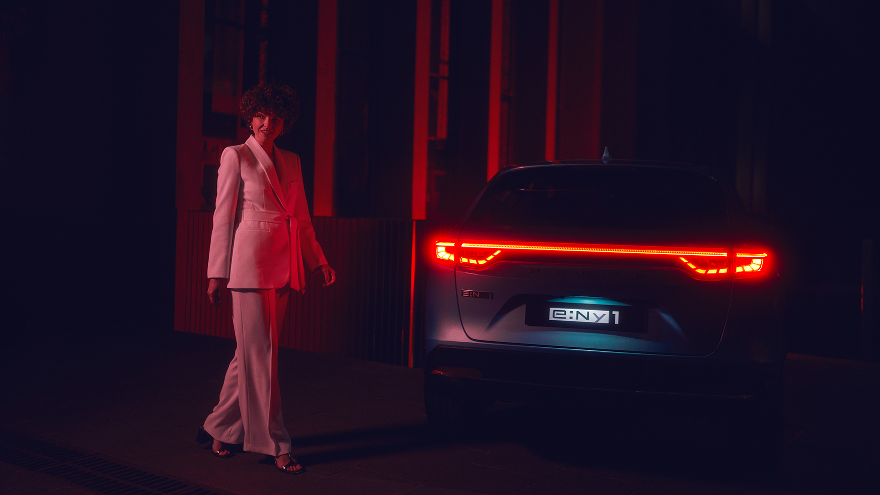 Model standing next to illuminated rear of the Honda e:Ny1 at night.