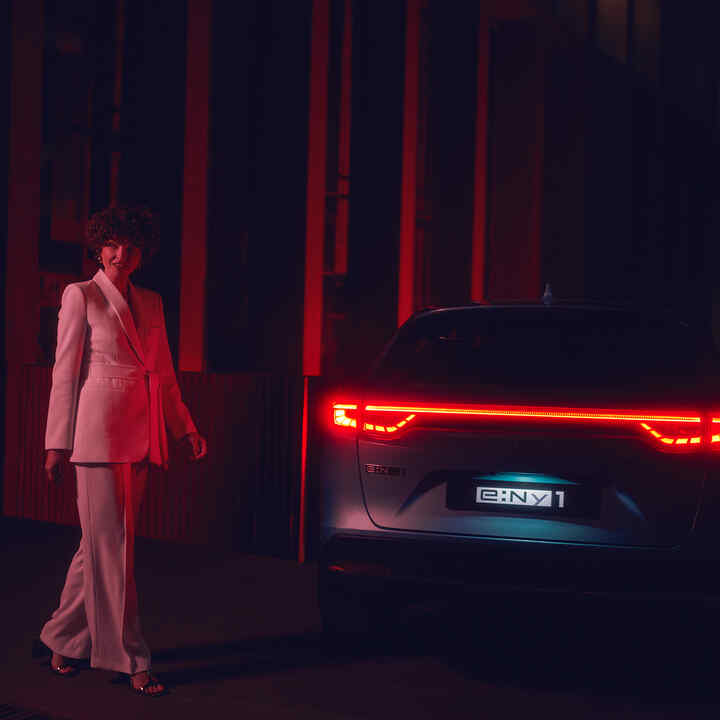 Model standing next to illuminated rear of the Honda e:Ny1 at night.