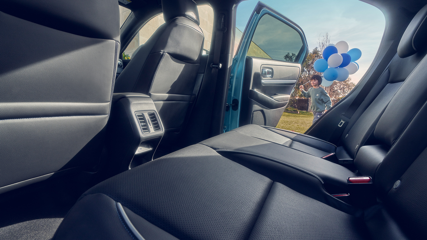 Close up of the rear seat in the Honda e:Ny1 with child walking past open door carrying balloons.