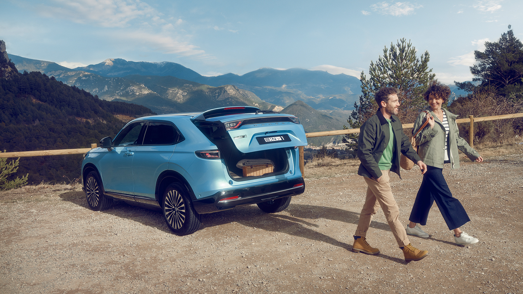 Rear facing three quarter Honda e:Ny1 in mountainous loacation with couple walking away.