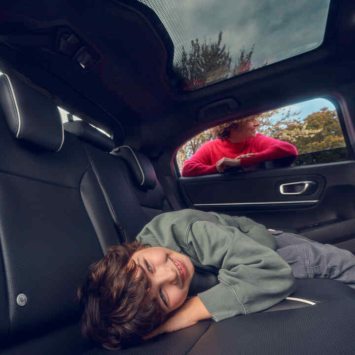 Child laying on the back seat with mother stands in the window of Honda e:Ny1.