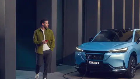 Man walking past a charging Honda e:Ny1 in front of a building.