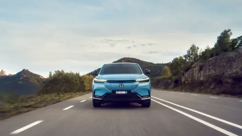 Front facing Honda e:Ny1 driving down the road in a mountainous location.