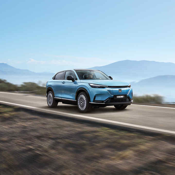 Front 3/4 facing Honda e:Ny1 electric SUV on the road with hills in the distance