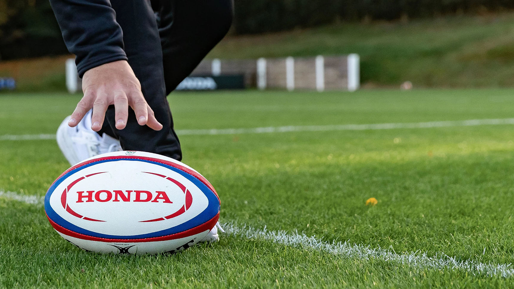 Rugby ball being picked up with Honda logo on. 