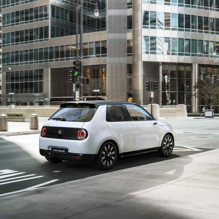 Rear facing three quarter Honda e driving through the city.