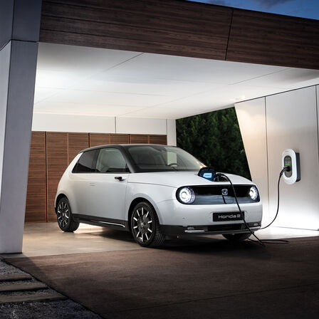 Front facing three quarter Honda e parked in the driveway charging as the owner enters the home.