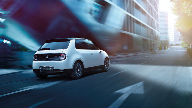 Front facing three quarter Honda e driving through an electrified city.