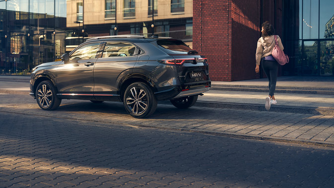 Honda HR-V SUV parked on the side of a street with a women walking behind it. 