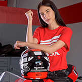 Lady wearing a red Honda Top leaning on a Honda motorcycle helmet.