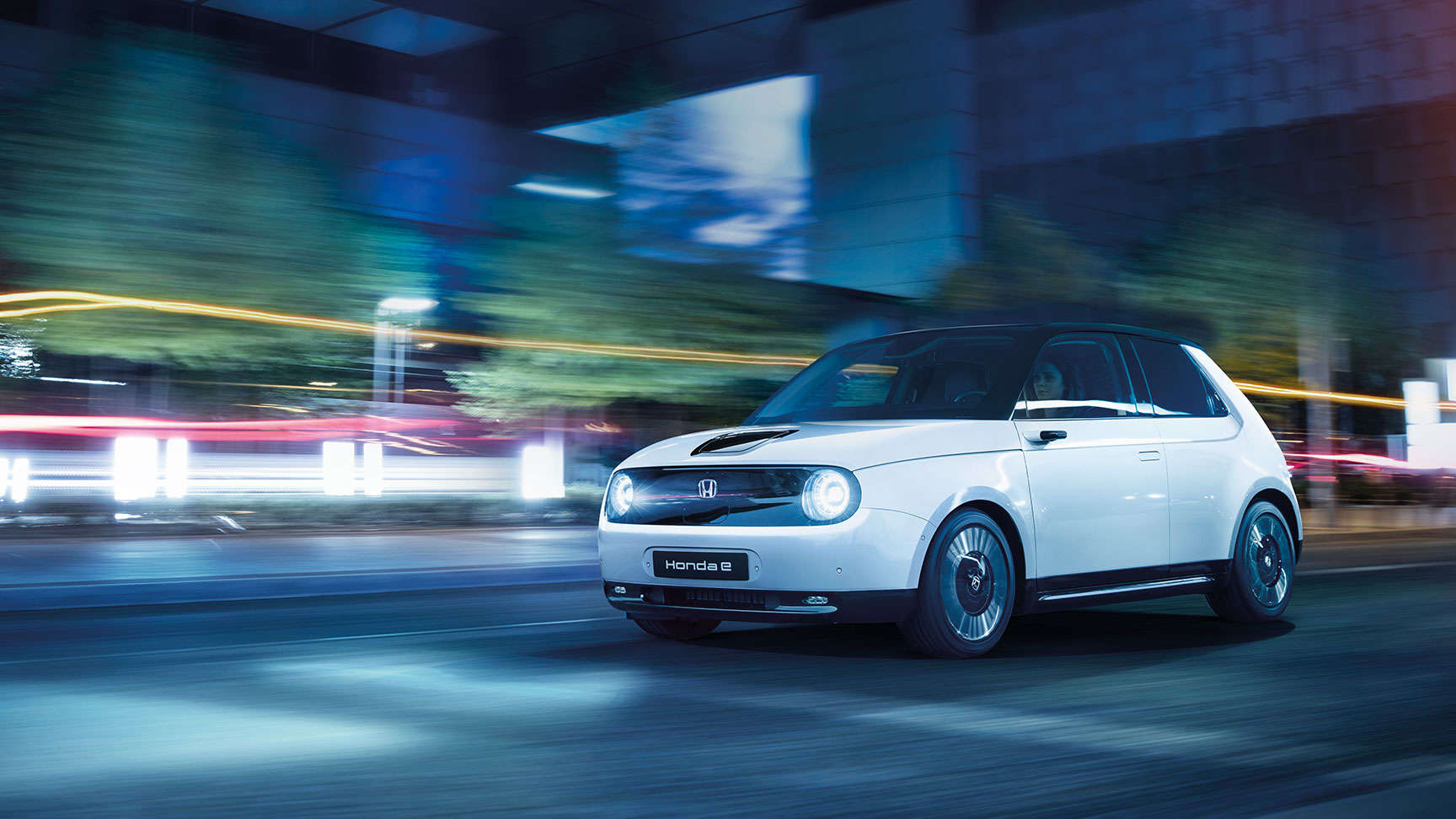 White Honda e driving through the city at night