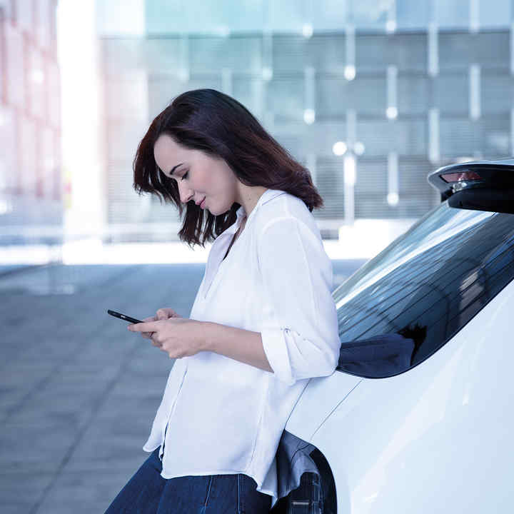 Lady Leaning against Rear of Honda e looking at phone