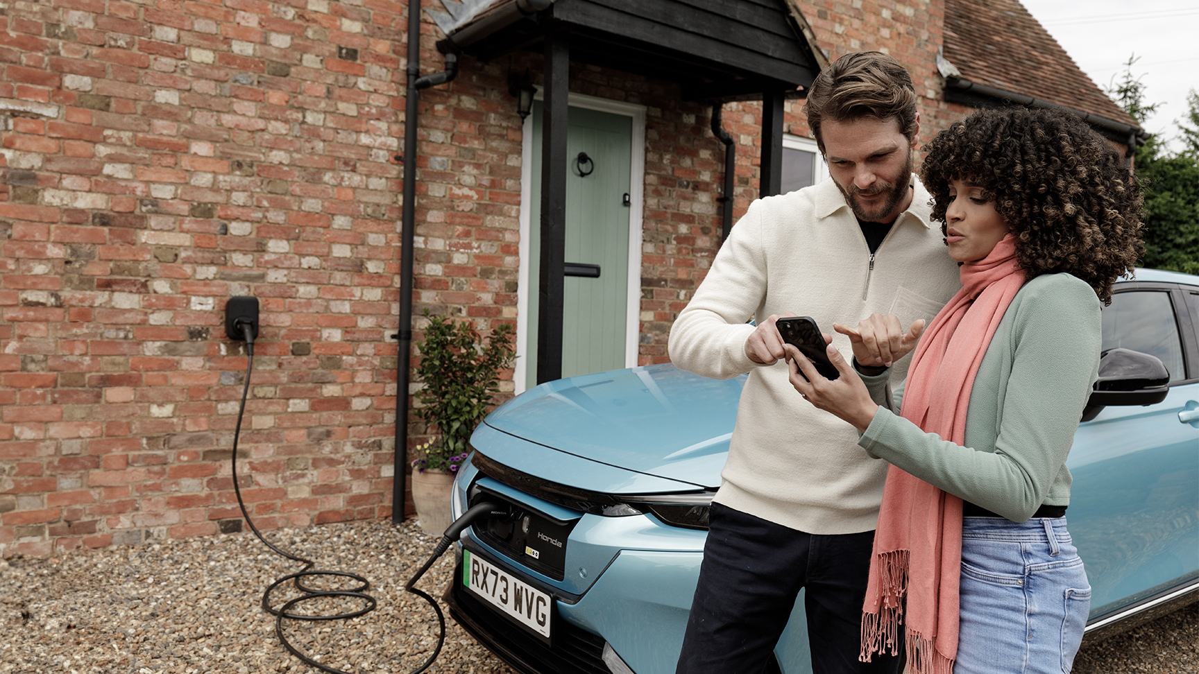 Model holding a phone with a close up of the Honda E charging system.