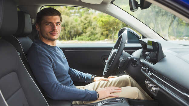 Max Verstappen sitting inside the ZR-V Hybrid SUV car in a park location.