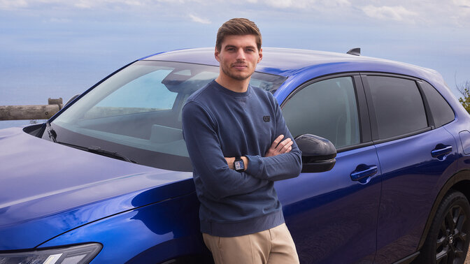 Max Verstappen leaning on blue Honda ZR-V Hybrid SUV car parked.