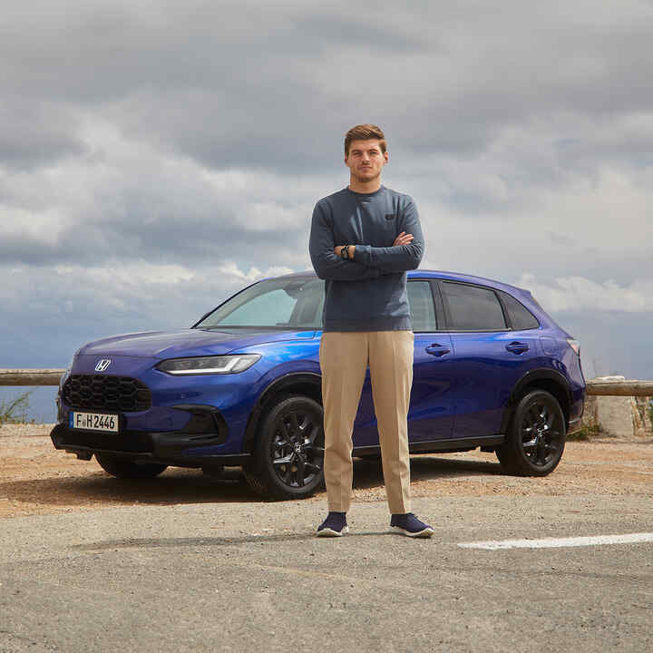 Max Verstappen standing next to a blue Honda ZR-V Hybrid Suv car.