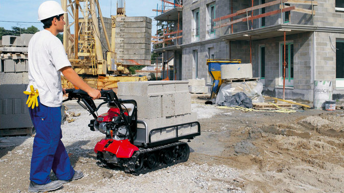 Power carrier being used by a worker in blue jeans and white helmet on a building site