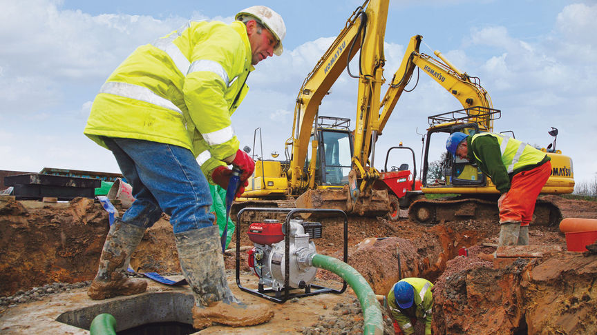 High flow rate water pump being used by worker on construction site.